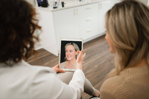 Provider and patient reviewing before-and-after photos discussing PRF under-eye treatment, Sculptra for jowls, and neck rejuvenation options.