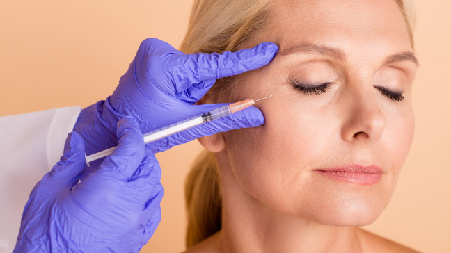 Provider in purple gloves administering a neurotoxin injection near a woman's eye area