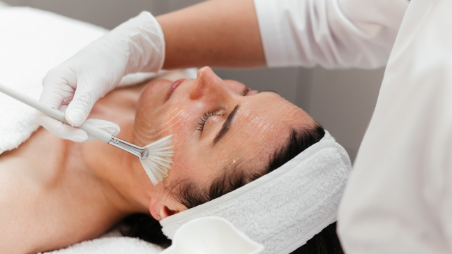 Esthetician applying a facial peel treatment with a brush to a woman's cheek.